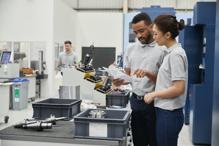 Engineer And Apprentice Meet On Floor Of Engineering Workshop